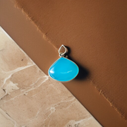 Close-up image of a natural Turquoise (Firoza) gemstone pendant with polished surface, paired with a black adjustable thread, displayed on a wooden background