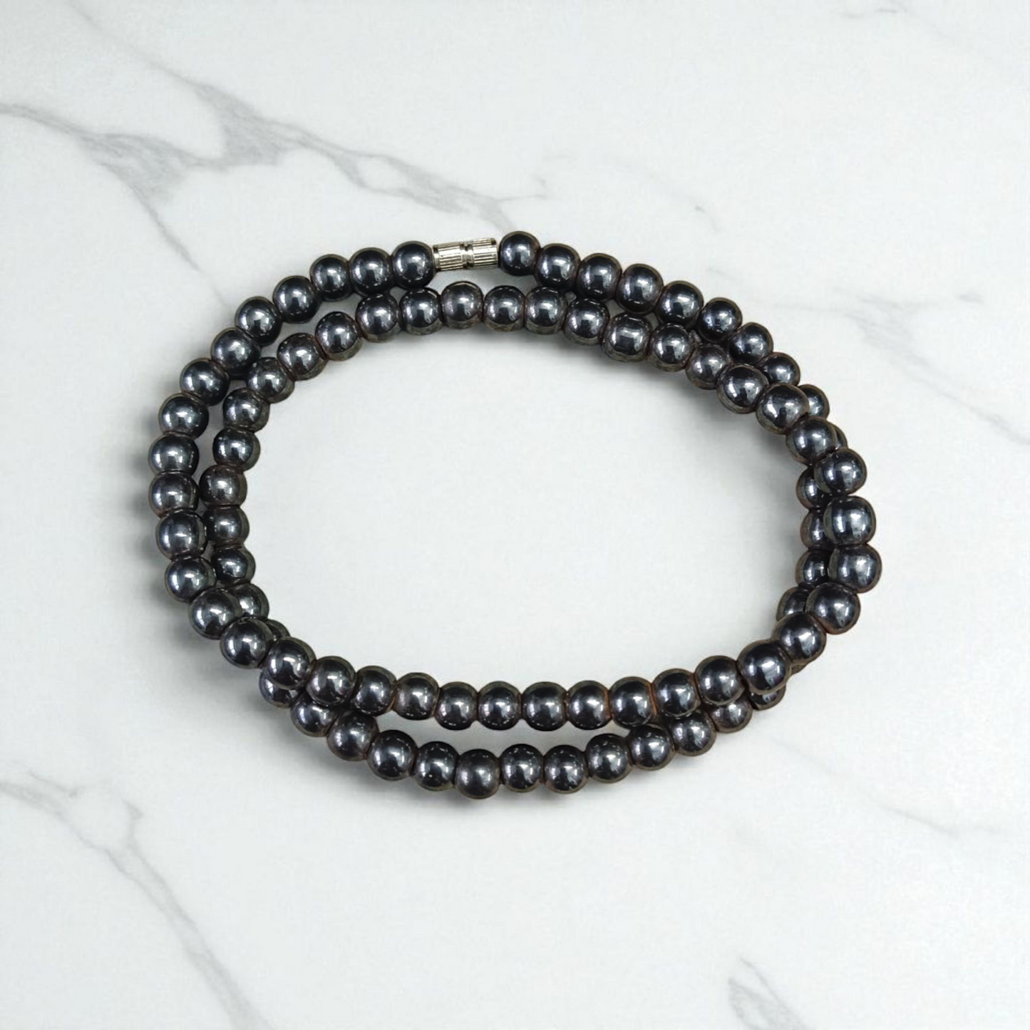 Image of Magnetic Mala made of black hematite beads, laid out in a spiral on a white background