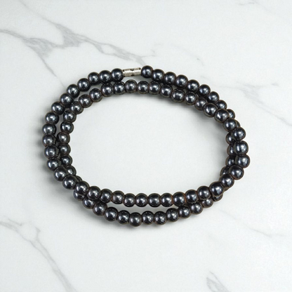 Image of Magnetic Mala made of black hematite beads, laid out in a spiral on a white background