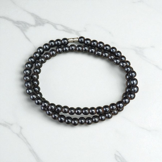 Image of Magnetic Mala made of black hematite beads, laid out in a spiral on a white background