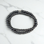 Image of Magnetic Mala made of black hematite beads, laid out in a spiral on a white background