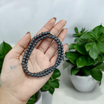 Image of Magnetic Mala made of black hematite beads, laid out in a spiral on a white background