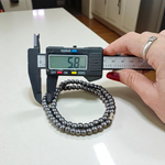 Image of Magnetic Mala made of black hematite beads, laid out in a spiral on a white background