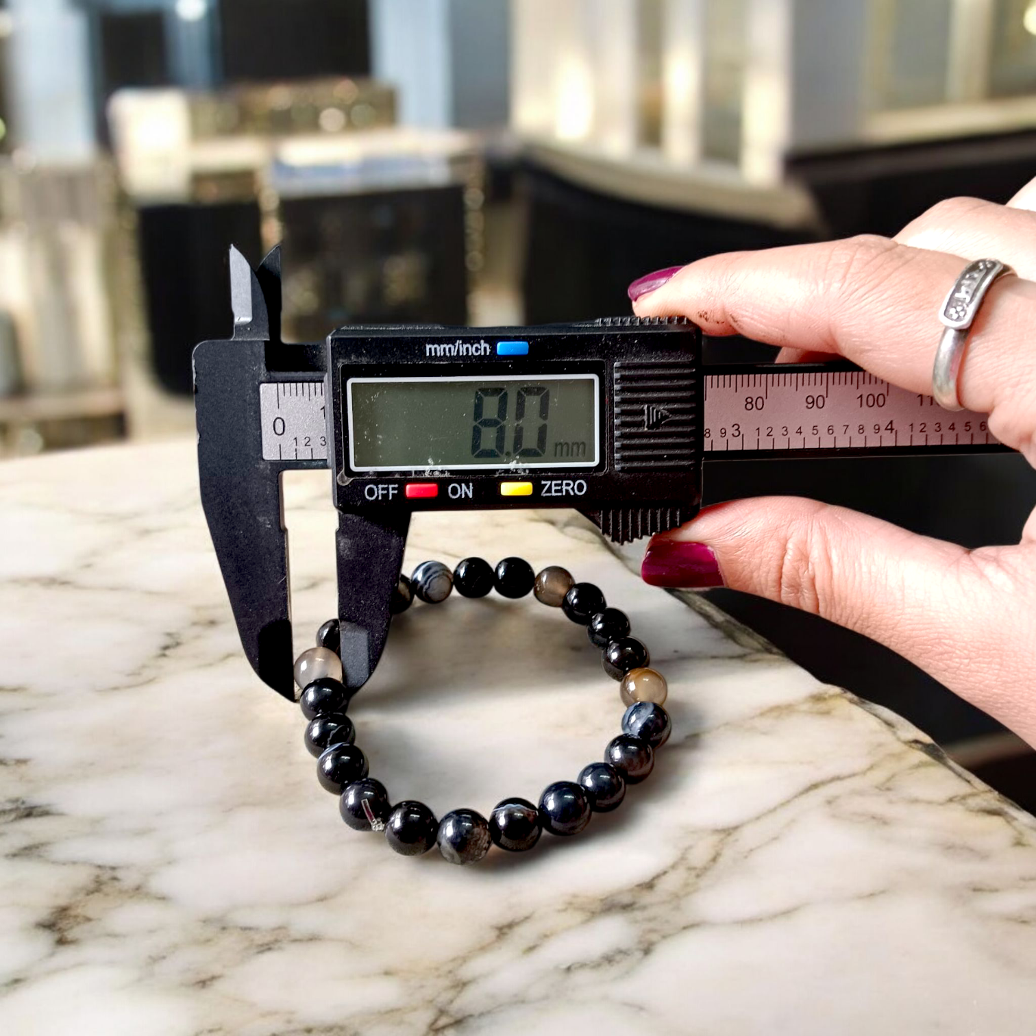 Image of Natural Sulemani Hakik Bracelet with 8mm round black agate beads in a stretchable design, displayed in a circular shape on a white surface