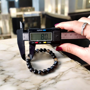 Image of Natural Sulemani Hakik Bracelet with 8mm round black agate beads in a stretchable design, displayed in a circular shape on a white surface