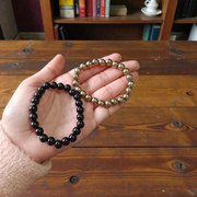 Image of a combo bracelet featuring 8mm golden Pyrite beads and glossy black Obsidian beads arranged side by side on a neutral background