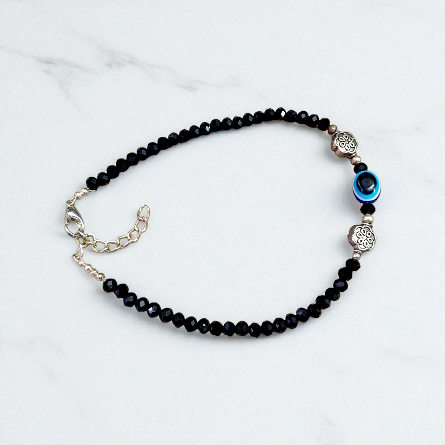 Image of a handcrafted black crystal beads anklet with a central evil eye charm, designed for unisex wear and spiritual protection