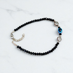 Image of a handcrafted black crystal beads anklet with a central evil eye charm, designed for unisex wear and spiritual protection