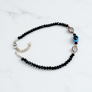 Image of a handcrafted black crystal beads anklet with a central evil eye charm, designed for unisex wear and spiritual protection