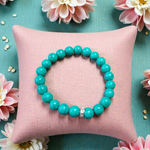Image of a natural turquoise bracelet with polished 8mm round blue beads and black veining, displayed in a circular shape on a plain background