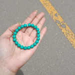 Image of a natural turquoise bracelet with polished 8mm round blue beads and black veining, displayed in a circular shape on a plain background