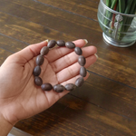 Image of two adjustable spiritual bracelets – one made with white Vaijanti seeds and the other with brown Kamal Gutta beads – displayed on a natural surface