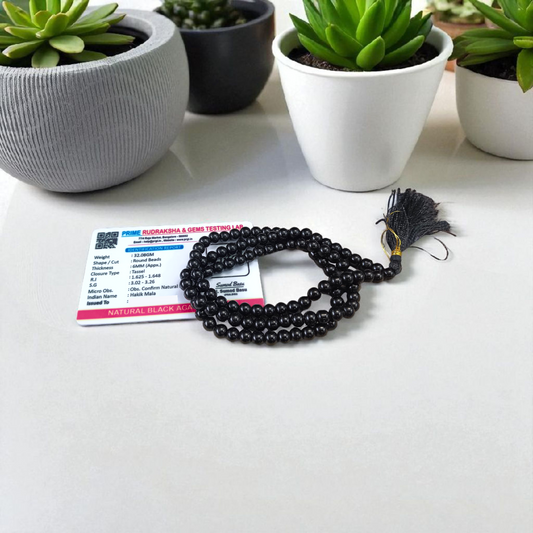 Natural Black Agate (Hakik) Mala made of 6mm smooth beads, coiled neatly with a Guru bead on a light background