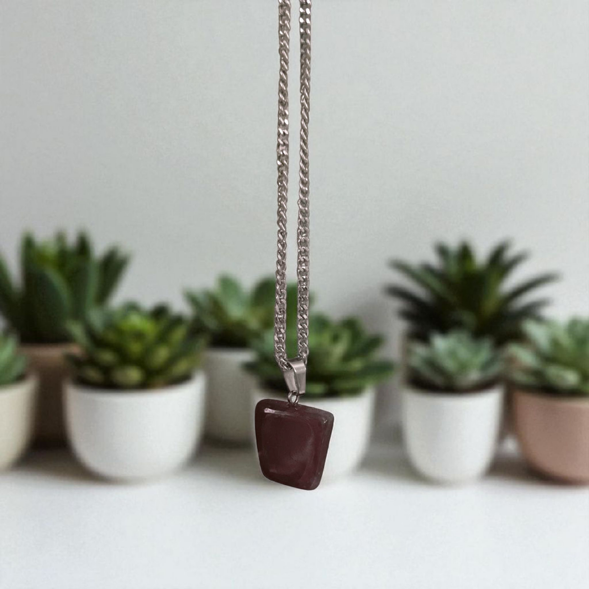 Polished deep red Almandine Garnet pendant with stainless steel chain, designed for men and women, displayed on a neutral surface