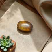 Polished natural brown Tiger Eye Stone with golden shimmer, placed on a white surface for healing and meditation purposes