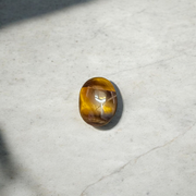 Polished natural brown Tiger Eye Stone with golden shimmer, placed on a white surface for healing and meditation purposes