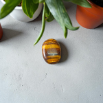 Polished natural brown Tiger Eye Stone with golden shimmer, placed on a white surface for healing and meditation purposes
