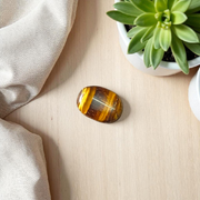 Polished natural brown Tiger Eye Stone with golden shimmer, placed on a white surface for healing and meditation purposes