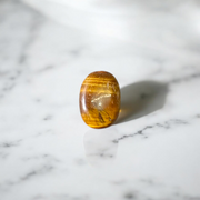 Polished natural brown Tiger Eye Stone with golden shimmer, placed on a white surface for healing and meditation purposes