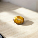 Polished natural brown Tiger Eye Stone with golden shimmer, placed on a white surface for healing and meditation purposes