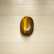Polished natural brown Tiger Eye Stone with golden shimmer, placed on a white surface for healing and meditation purposes