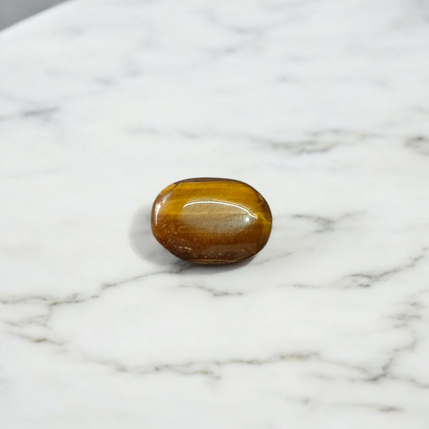 Polished natural brown Tiger Eye Stone with golden shimmer, placed on a white surface for healing and meditation purposes
