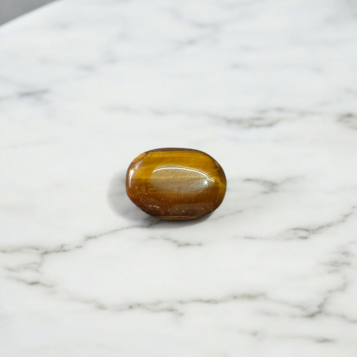 Polished natural brown Tiger Eye Stone with golden shimmer, placed on a white surface for healing and meditation purposes
