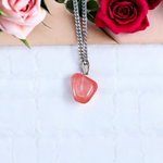 Polished rose quartz tumble pendant with silver chain, displayed on a neutral background, highlighting soft pink color and smooth finish