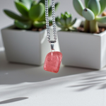 Polished rose quartz tumble pendant with silver chain, displayed on a neutral background, highlighting soft pink color and smooth finish