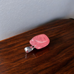 Polished rose quartz tumble pendant with silver chain, displayed on a neutral background, highlighting soft pink color and smooth finish