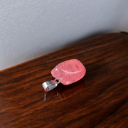 Polished rose quartz tumble pendant with silver chain, displayed on a neutral background, highlighting soft pink color and smooth finish