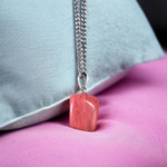 Polished rose quartz tumble pendant with silver chain, displayed on a neutral background, highlighting soft pink color and smooth finish