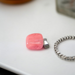 Polished rose quartz tumble pendant with silver chain, displayed on a neutral background, highlighting soft pink color and smooth finish
