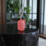 Polished rose quartz tumble pendant with silver chain, displayed on a neutral background, highlighting soft pink color and smooth finish