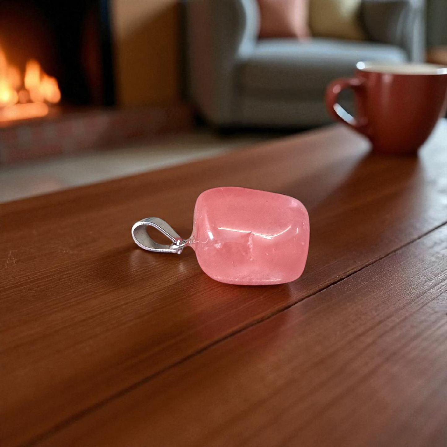 Polished rose quartz tumble pendant with silver chain, displayed on a neutral background, highlighting soft pink color and smooth finish