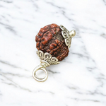 Rudraksha Ganesh Pendant with natural brown beads and silver-coated Ganesha idol, placed on a spiritual-themed background