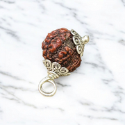 Rudraksha Ganesh Pendant with natural brown beads and silver-coated Ganesha idol, placed on a spiritual-themed background