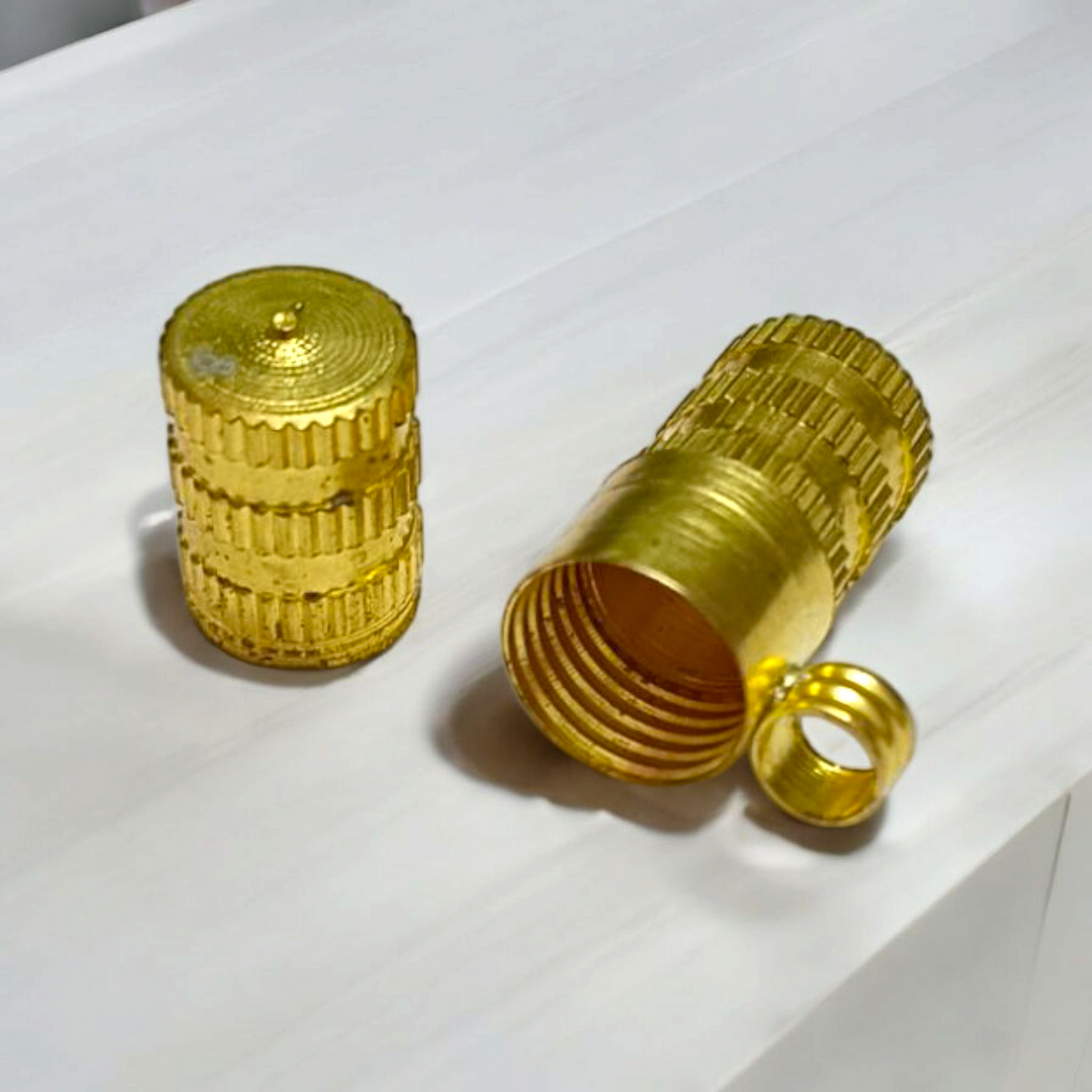 Set of five golden metal taweez cylinders placed neatly beside rolled Bhojpatra sheets on a white surface