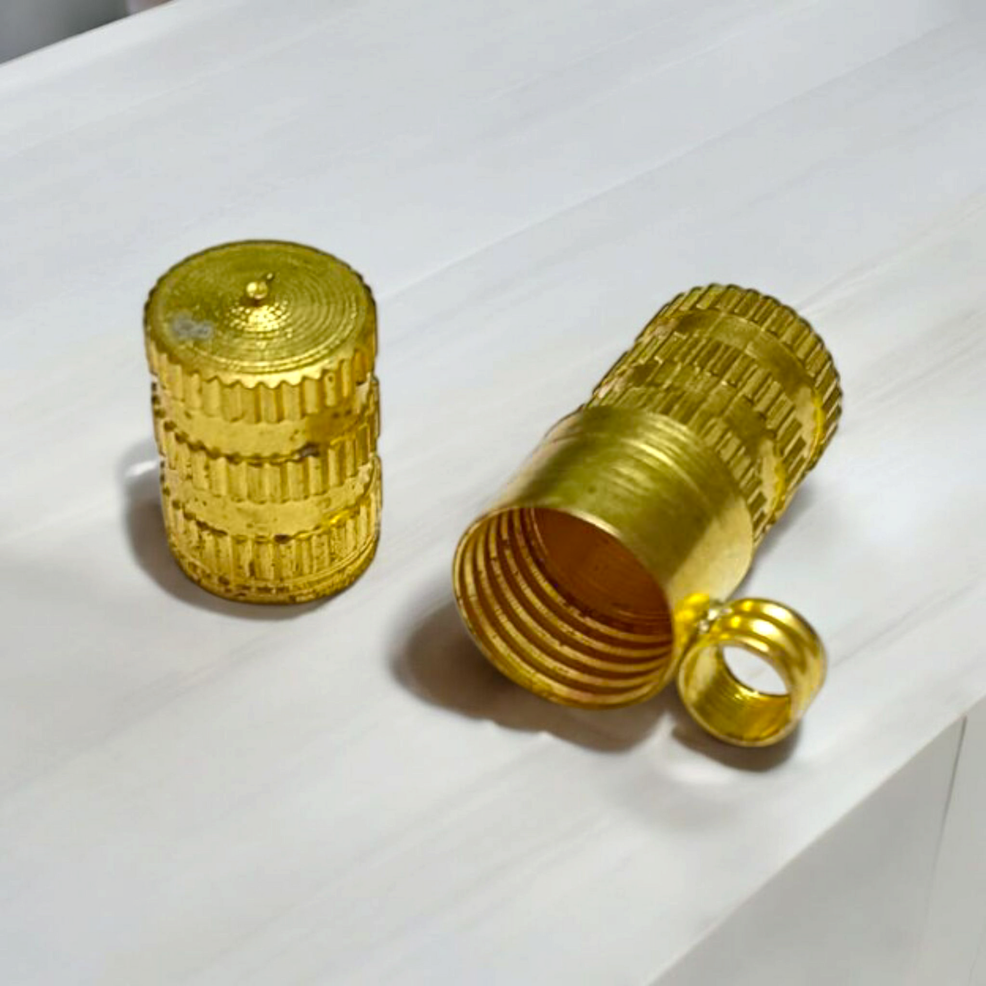 Set of five golden metal taweez cylinders placed neatly beside rolled Bhojpatra sheets on a white surface