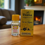 Small glass vial of 2ML Sandal Attar by Veena, MALAWALA brand, with golden cap and traditional label, placed on a wooden background with sandalwood chips