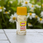 Small glass vial of 2ML Sandal Attar by Veena, MALAWALA brand, with golden cap and traditional label, placed on a wooden background with sandalwood chips