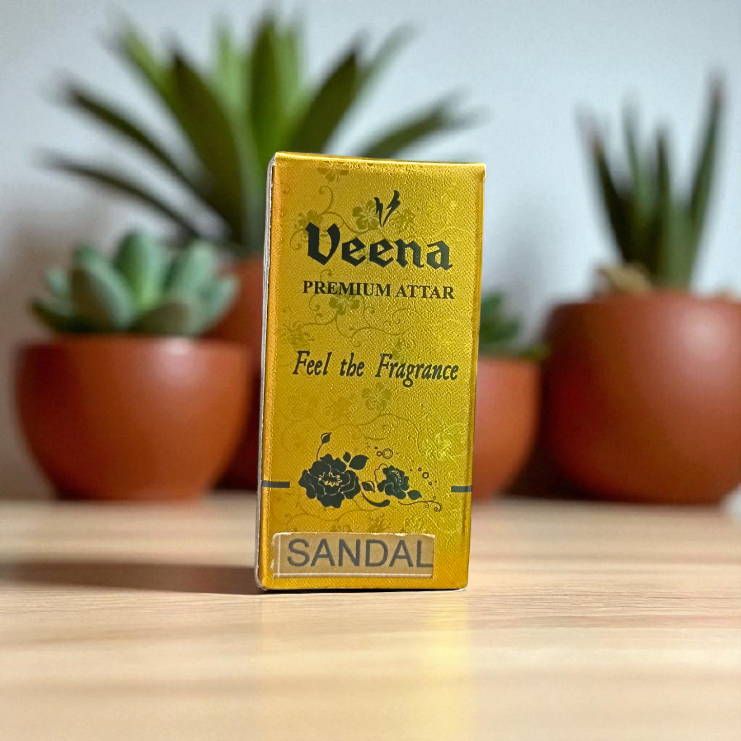 Small glass vial of 2ML Sandal Attar by Veena, MALAWALA brand, with golden cap and traditional label, placed on a wooden background with sandalwood chips
