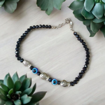 Unisex black crystal beads anklet featuring protective Evil Eye and lucky Fish charms, handcrafted for spiritual style and daily wear